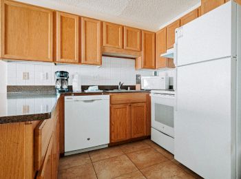 The image shows a kitchen with wooden cabinets, white appliances including a refrigerator, stove, dishwasher, and a microwave. There’s also a coffee maker.