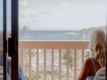 A couple holding hands sits on a balcony, gazing at a scenic ocean view on a sunny day.