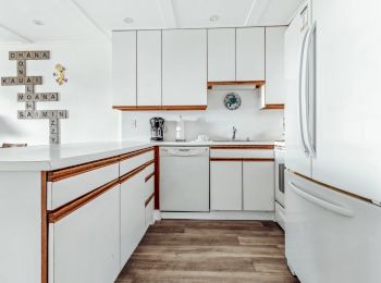 A modern white kitchen with wooden accents, featuring a large fridge, dishwasher, and decorative blocks spelling words on the wall.