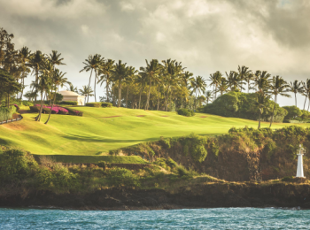 The image shows a scenic view of a coastal golf course with lush green fairways, palm trees, a lighthouse, and cliffs overlooking the ocean.