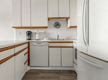 This image shows a modern kitchen with white cabinets, a refrigerator, a dishwasher, a coffee maker, and a sink, all set on a wooden floor.